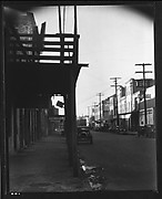 [Parked Cars and Warehouse Buildings on Cobblestone Street With Colonnade in Foreground, New Orleans, Louisiana?]