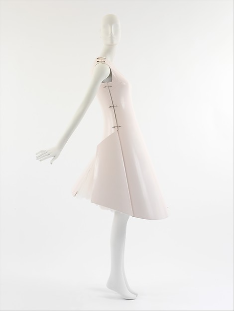 The pale pink dress on a white mannequin seen from the side, arm extended, with the rear flap lifted away from the skirt and a haze of tulle showing beneath.