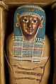 Mummy of Tasheriteniset with mummy mask and other cartonnage elements, also with garland of plants, Mummified human body, linen, mummification material, painted and gilded cartonnage, plant remains