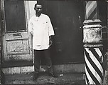 [Barber in White Coat Standing on Street Beside Striped Pole at Entrance to Shop, New York], Leon Levinstein  American, Gelatin silver print