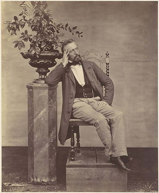 [Mathias Häusermann seated with elbow on pedestal holding a vase of flowers]
