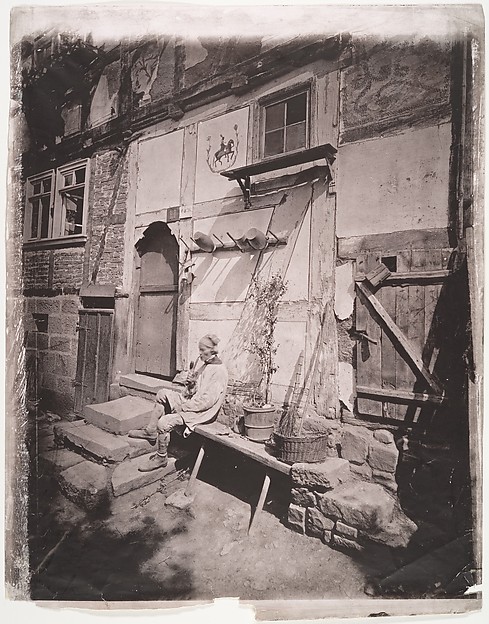 [Man Smoking Pipe Outside His Home on Village Street]