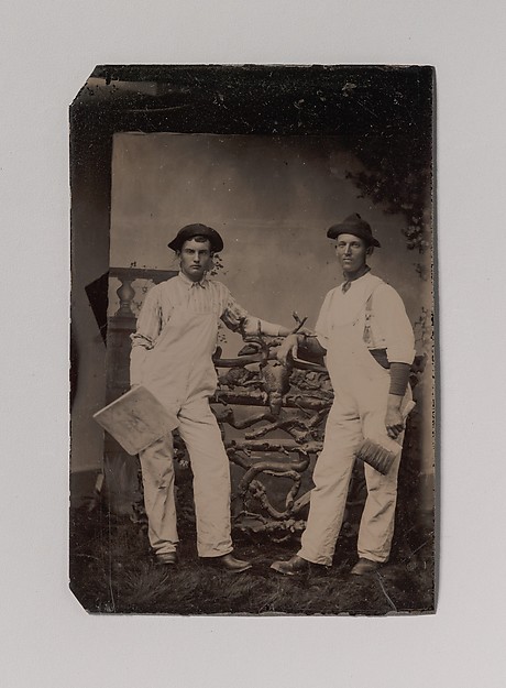 [Two Plasterers in Overalls Leaning on a Rustic Fence]